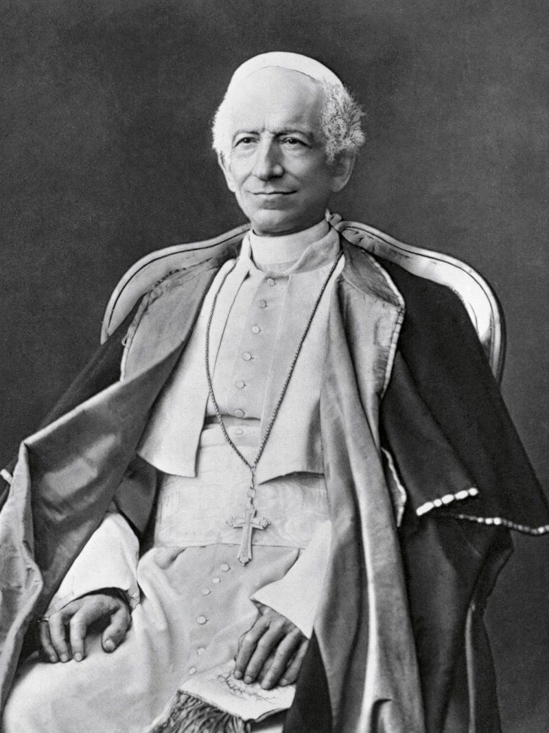 A photograph of Pope Leo XIII, seated, in white cassock and red cape.