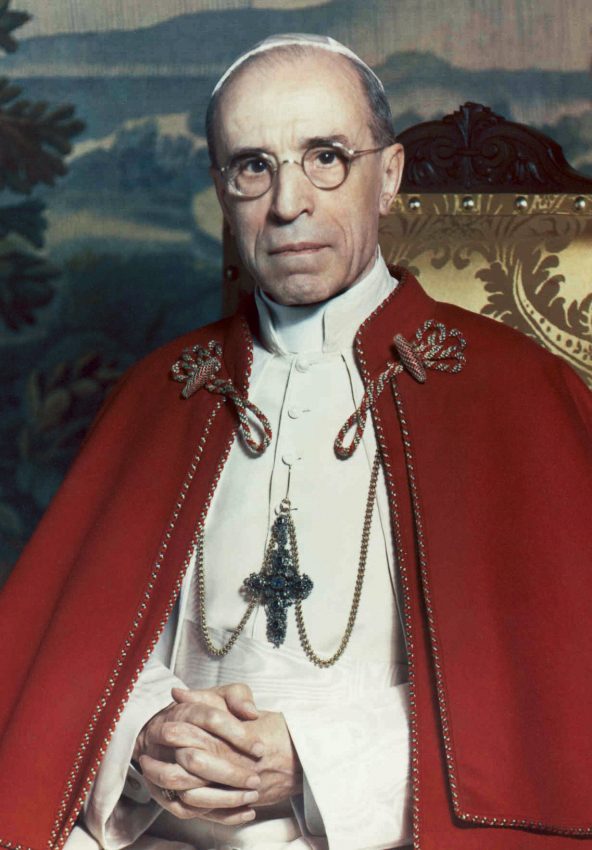 A photograph of Pope Pius XII in 1951, seated in red mozzetta, wearing round glasses.