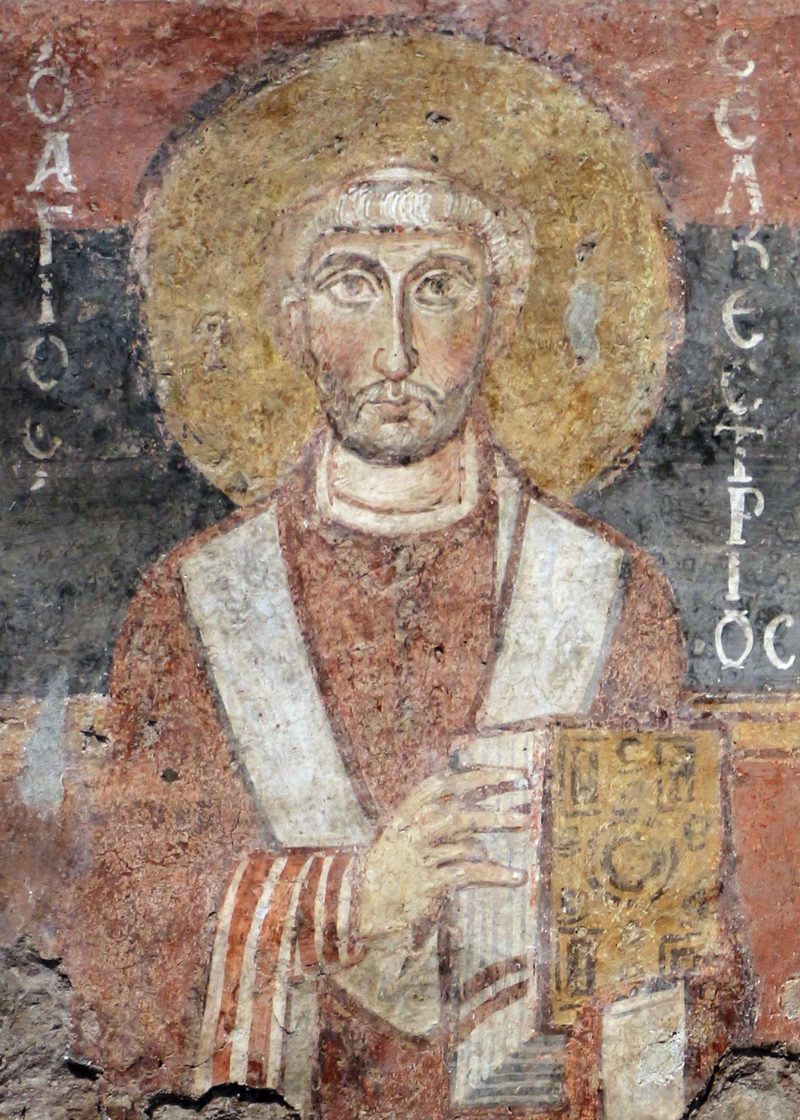 An early medieval fresco of a pope in white robes with a halo, holding a book.