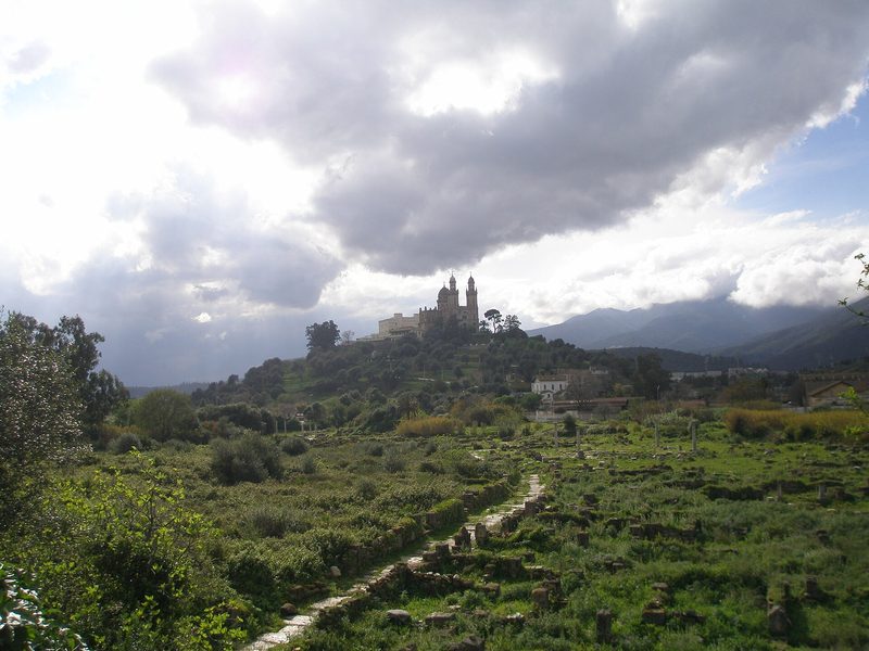 The ruins of ancient Hippo Regius near Annaba, Algeria, among green trees, with the Basilica of St Augustine on the hill beyond.