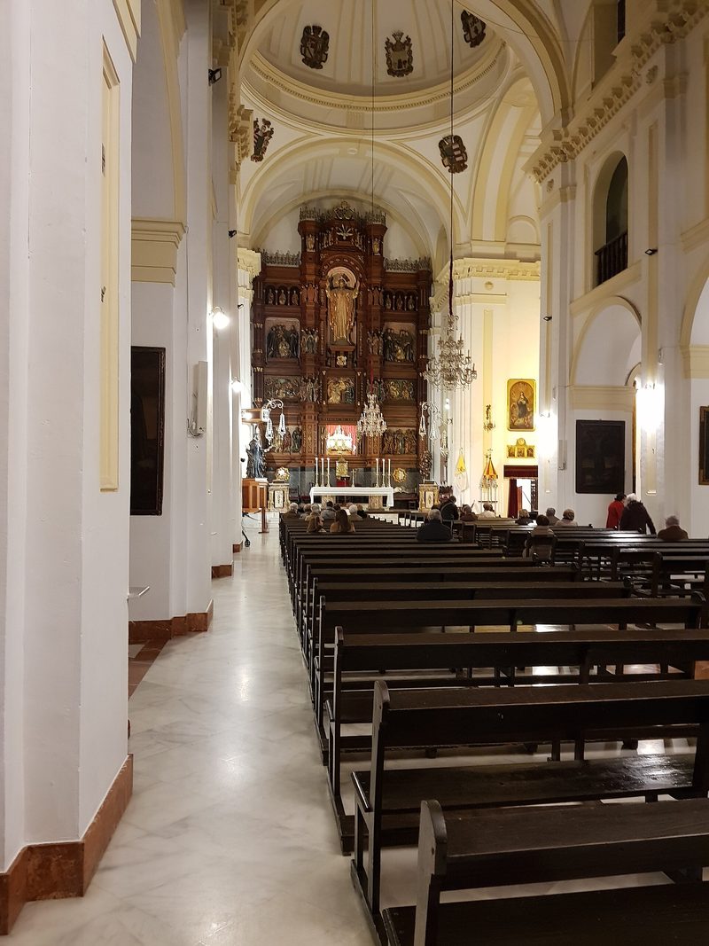Inside the Basilica of St John of Avila at Montilla: white walls, rows of pews and a gilded altarpiece.
