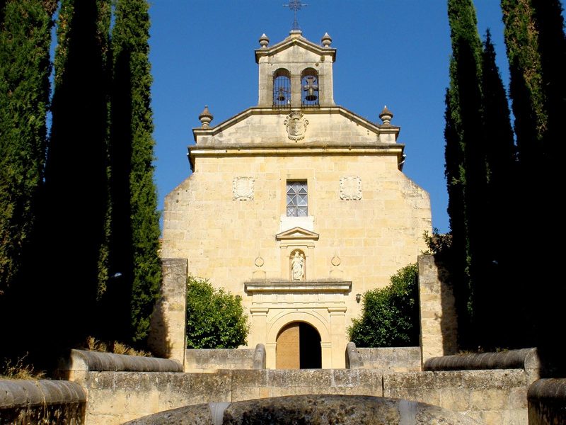 The Carmelite friary of Segovia: a pale stone church façade behind tall cypress trees.