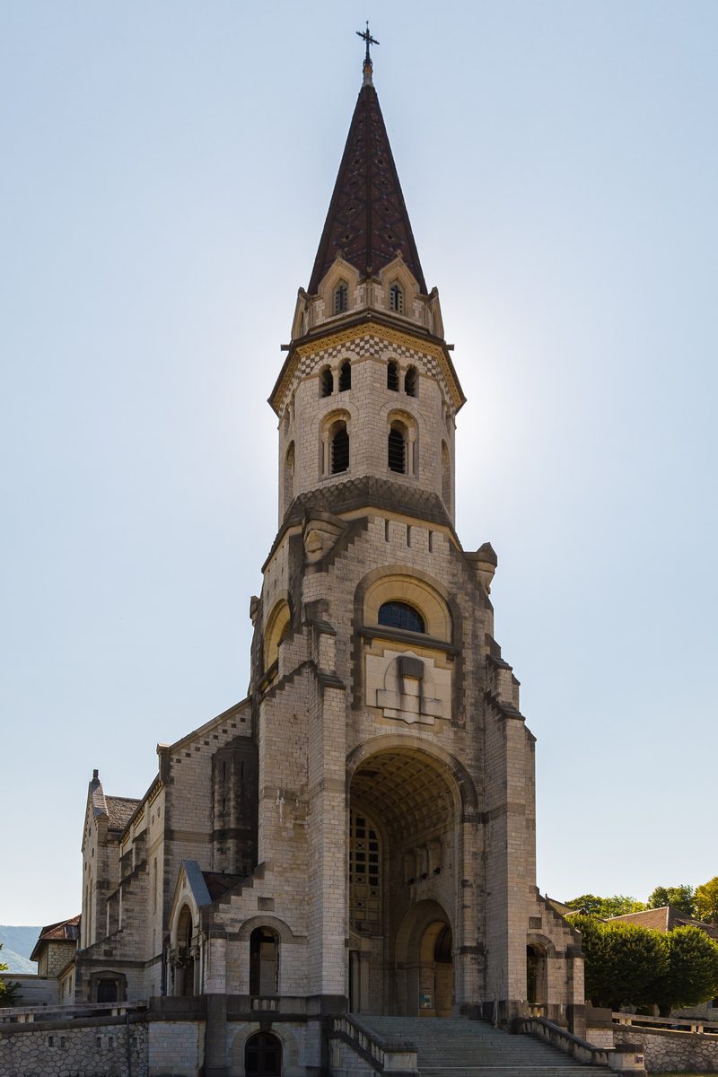The Basilica of the Visitation at Annecy: a pale stone church with a tall pointed spire against a blue sky.