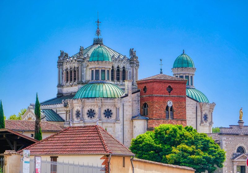 The Basilica of Ars-sur-Formans: a modern dome and an older bell tower above red tiled roofs.